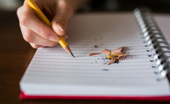 person holding pencil writing on notebook